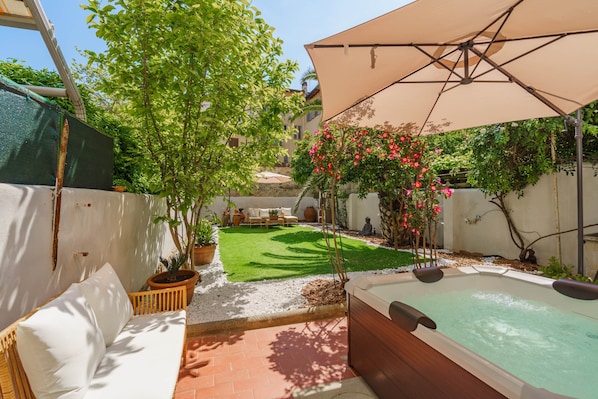 Un espace patio comprenant un jacuzzi, du mobilier d’extérieur, un arbre et un coin salon abrité.
