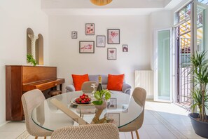 A dining area with a glass table, chairs, a piano, and a sofa with orange cushions.