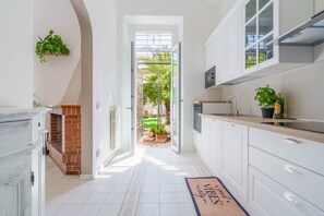 A modern kitchen with white cabinets, a brick fireplace, and a view to a garden.