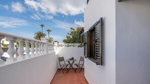 Een balkon met een witte reling, een tafel met twee stoelen en een raam met luiken.