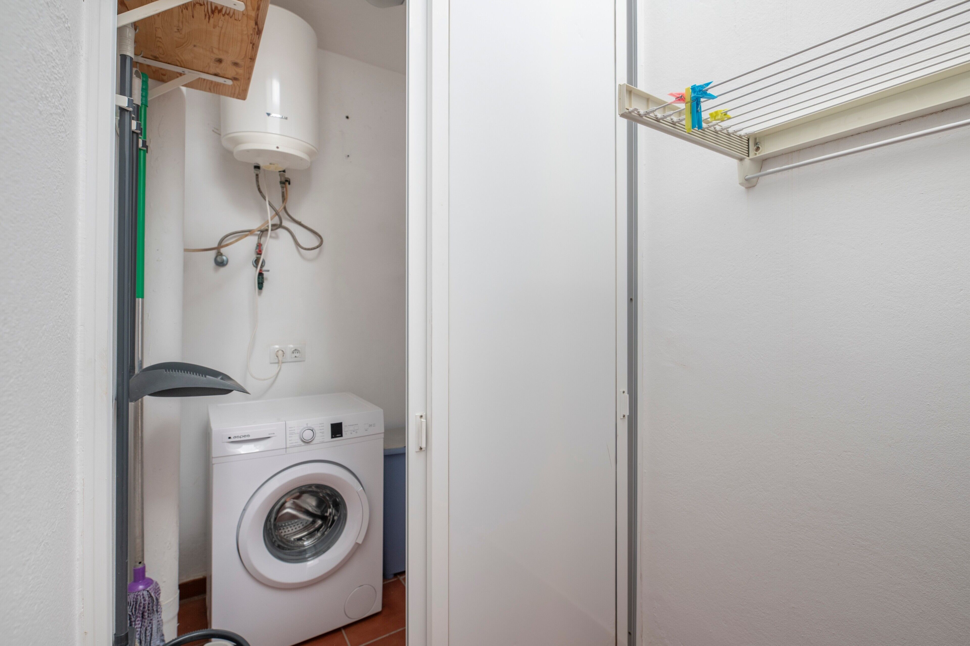 Een kleine wasruimte met een wasmachine, een droogrek en een heater aan het plafond.