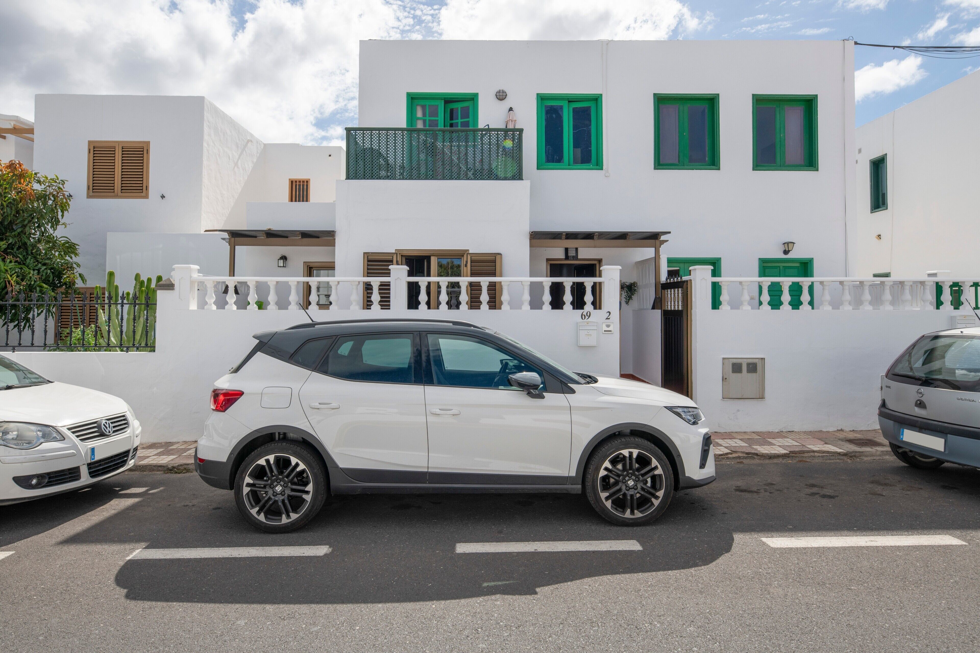 En hvid SUV parkeret foran en hvid bygning med grønne vinduesrammer og en balkon.