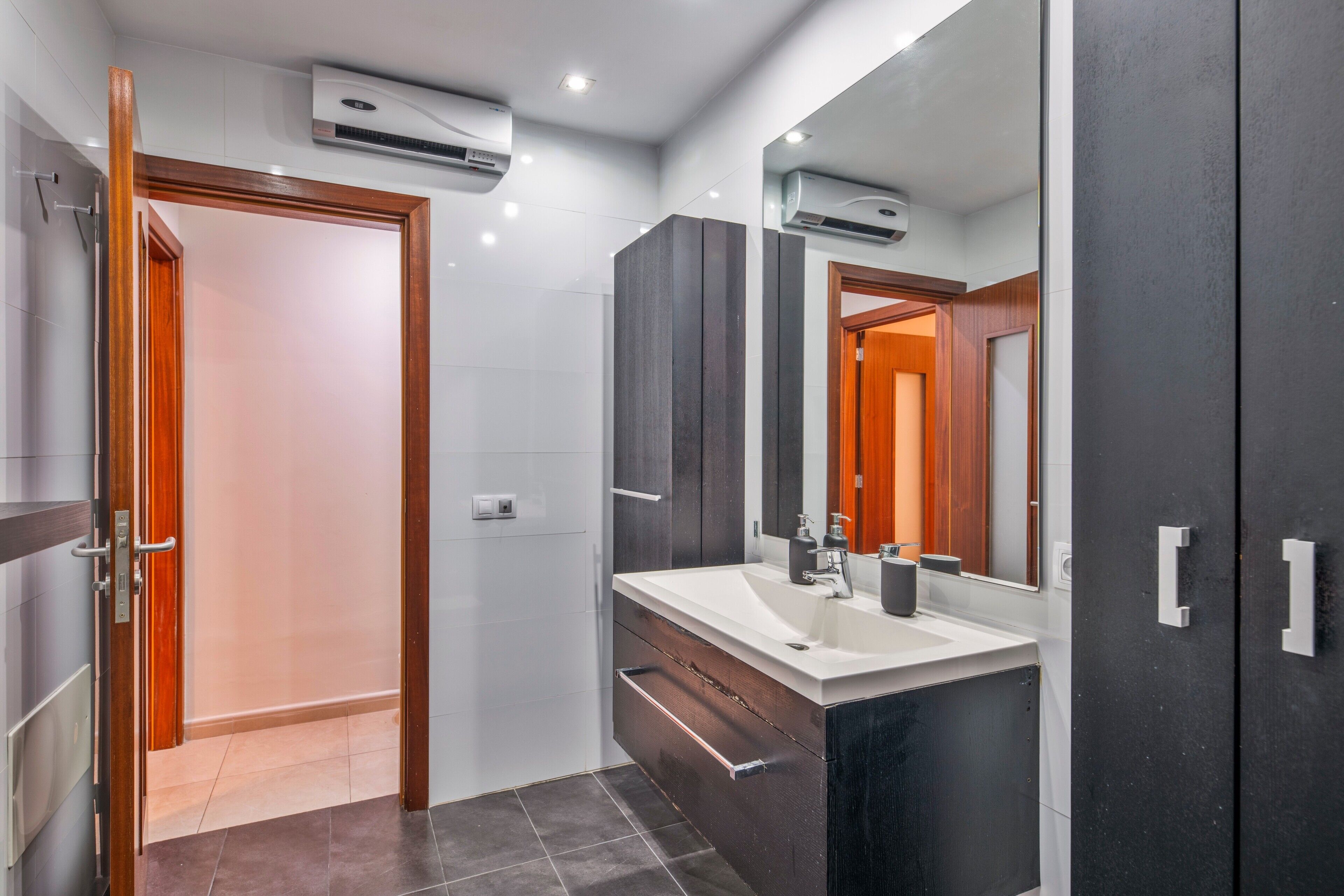 A modern bathroom with a large mirror, a sink, and dark cabinetry.