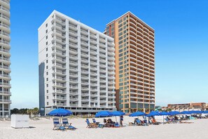 A hotel with multiple balconies, a beach area with sun loungers, and umbrellas. - Corner Condo - 3 bedroom/3 bath - Beautiful direct view of Gulf of America (Gulf Shores)