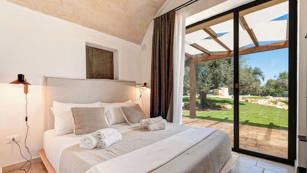 A bedroom with a large bed, a view of the garden, and a ceiling with exposed beams. - Le Camere di Corte Kalia by Raro Rooms (Francavilla Fontana)