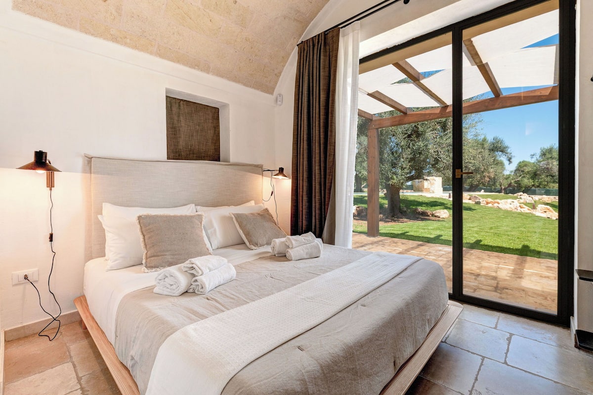 A bedroom with a large bed, a view of the garden, and a ceiling with exposed beams.