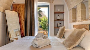 A bedroom with a bed, towels, a wooden headboard, a shelf with a kettle, and a view of the outdoors. - Le Camere di Corte Kalia by Raro Rooms (Francavilla Fontana)