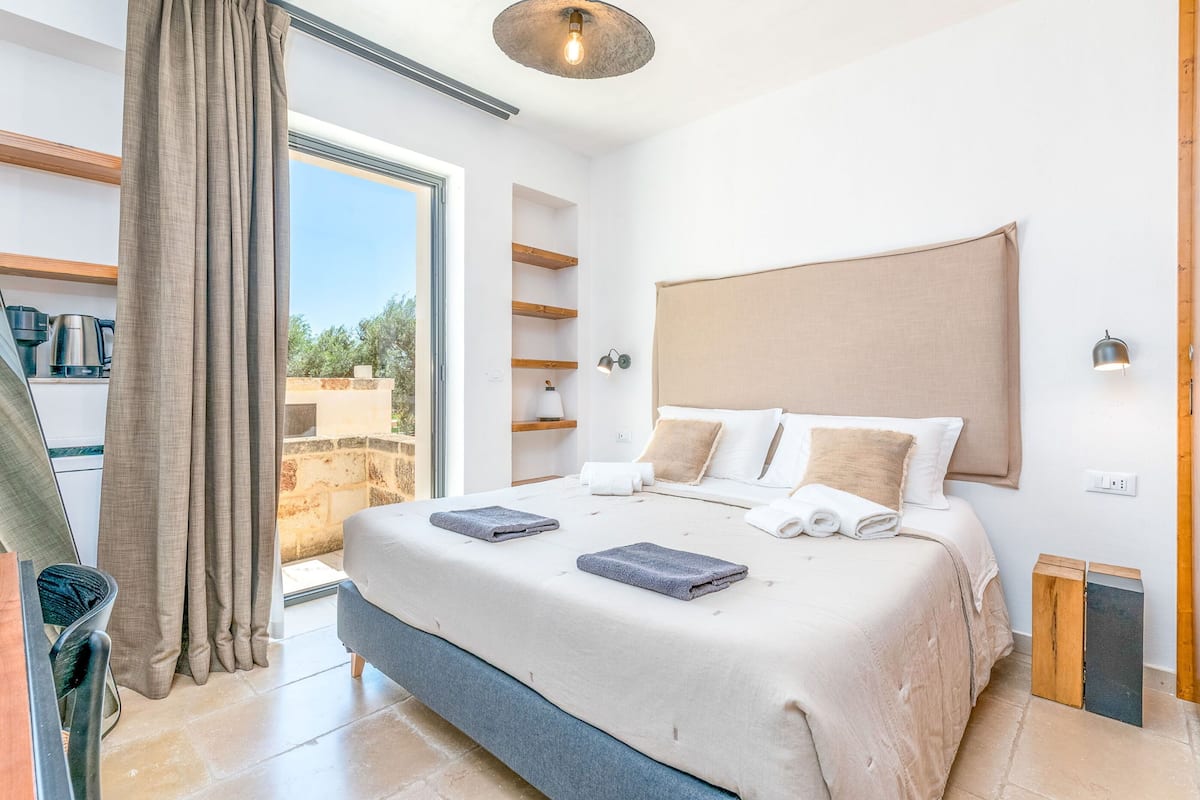 A bedroom with a large bed, a view through a sliding door, and a coffee maker on the left.