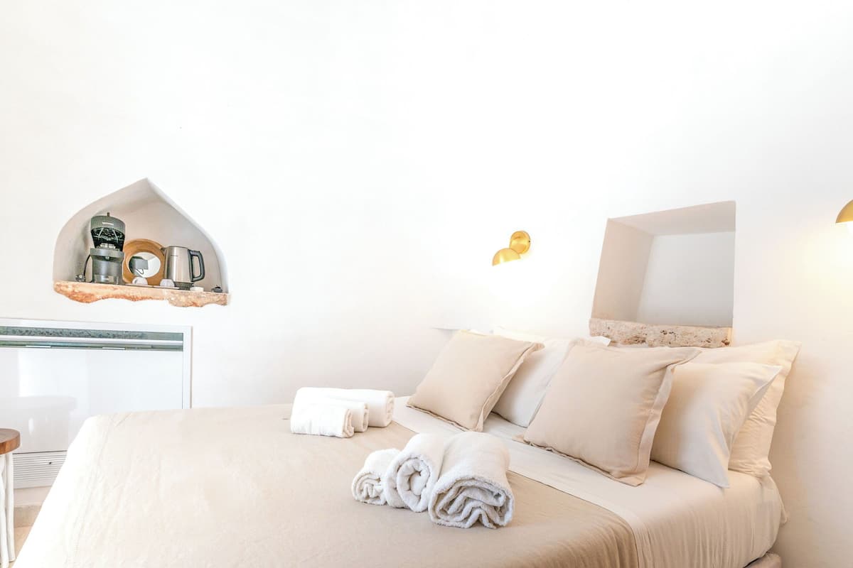 A hotel room with a bed, pillows, a coffee machine, and a mirror.