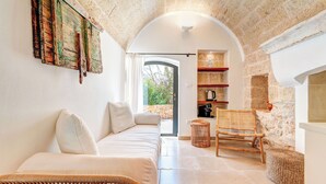A cozy interior with a sofa, wicker chair, stone walls, and a view through an archway. - Le Camere di Corte Kalia by Raro Rooms (Francavilla Fontana)