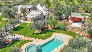 A large swimming pool with a curved design, surrounded by a well-maintained lawn and trees. - Le Camere di Corte Kalia by Raro Rooms (Francavilla Fontana)