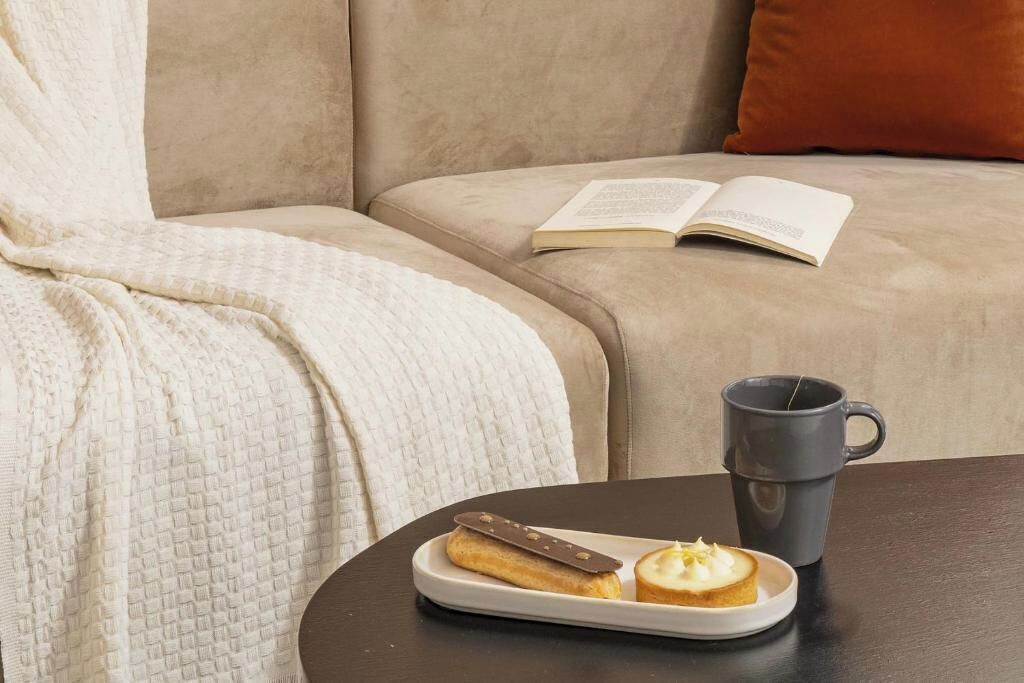 Ein gemütliches Wohnzimmer mit einer Couch, einem Couchtisch, einem Buch und einer Platte mit Gebäck.