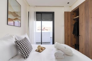 Hotellihuone, jossa on sänky, puinen vaatekaappi, ikkuna, josta on näkymä, ja seinällä oleva kehystetty taulu.