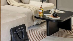 Un salon moderne avec un canapé, une table basse, un sac à main noir et un tapis à motifs.