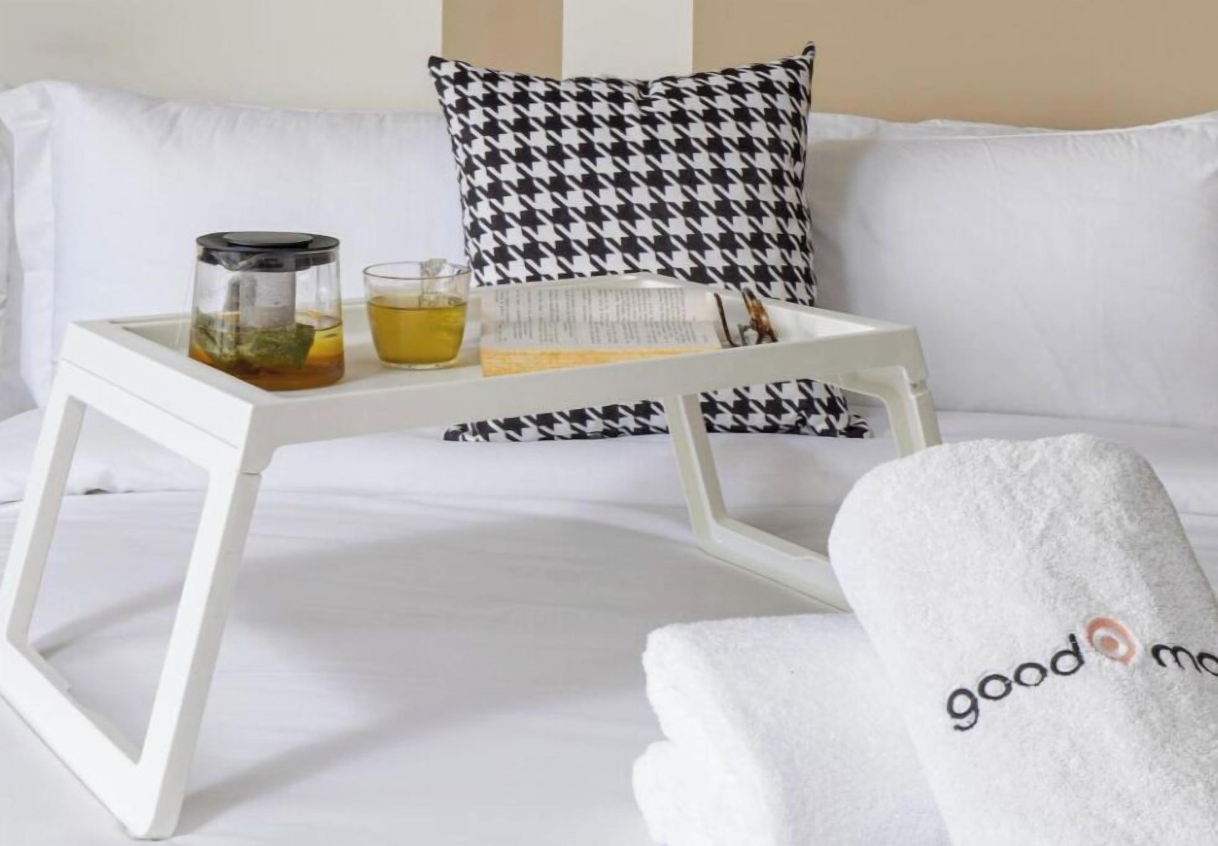 A white sofa with a houndstooth pillow, a tray with a tea pot, a glass of tea, and a towel with 'good morning' text.