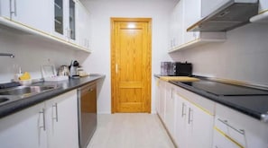 A narrow kitchen with white cabinets, a wooden door, and a black countertop. - Central | 3 BR | Easy Parking | Ideal for Groups (Granada)