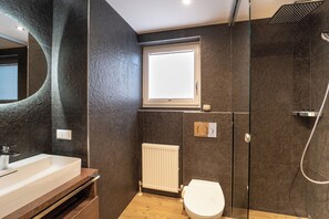 A modern bathroom with a large mirror, a white bathtub, a toilet, and a shower area. - das mondsee (Mondsee)