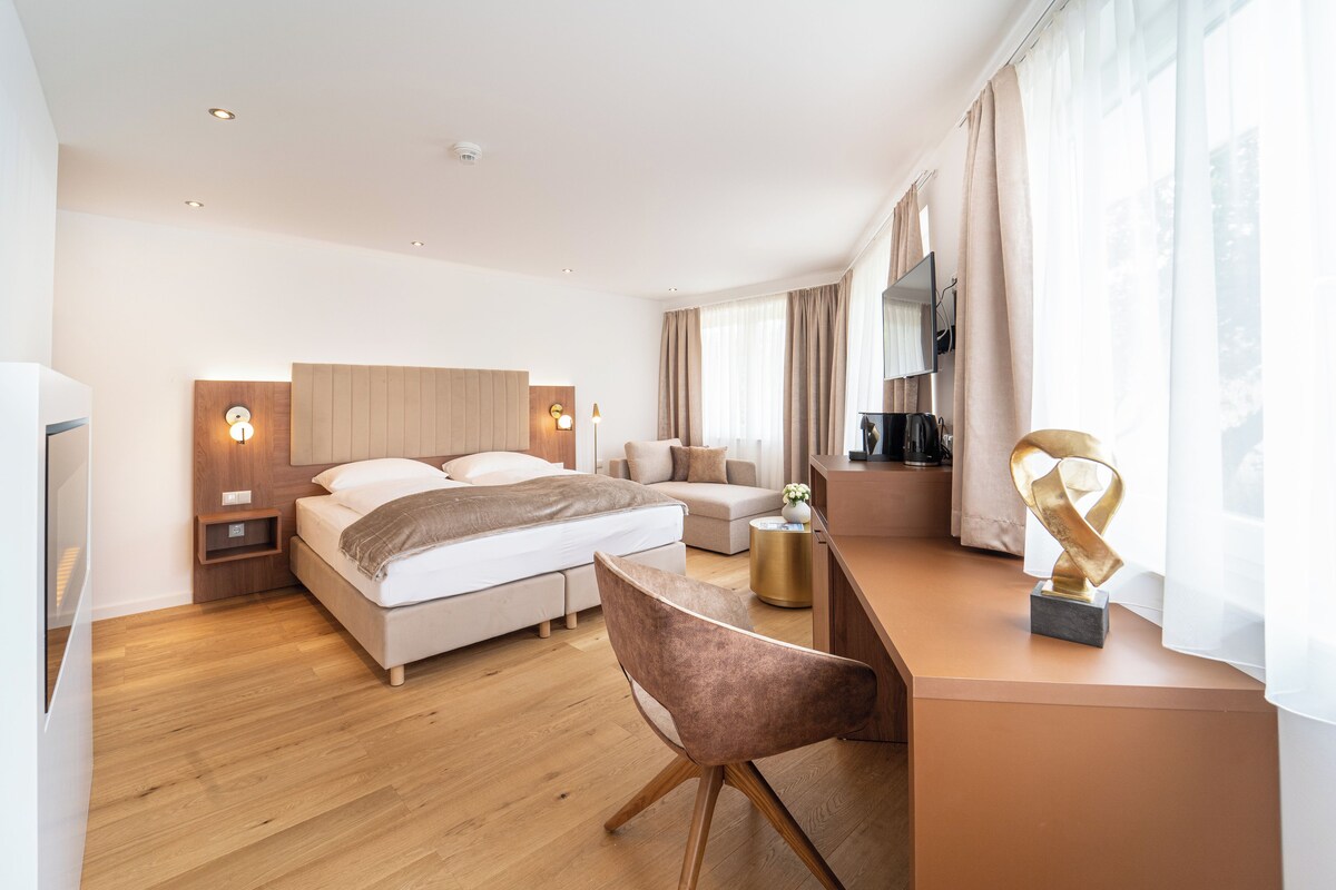 A modern hotel room with a bed, a sofa, a desk, and a chair.