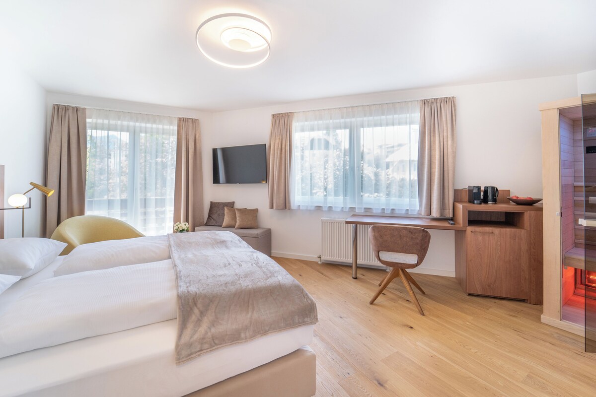 A hotel room with a bed, a desk, a chair, a TV, and a view of the outside.