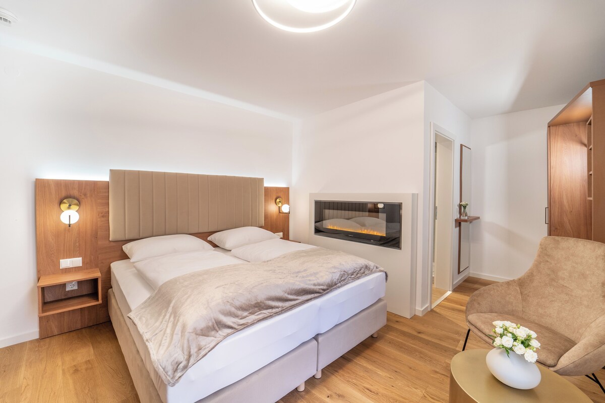 A modern bedroom with a bed, bedside tables, a wall-mounted TV, and a chair.