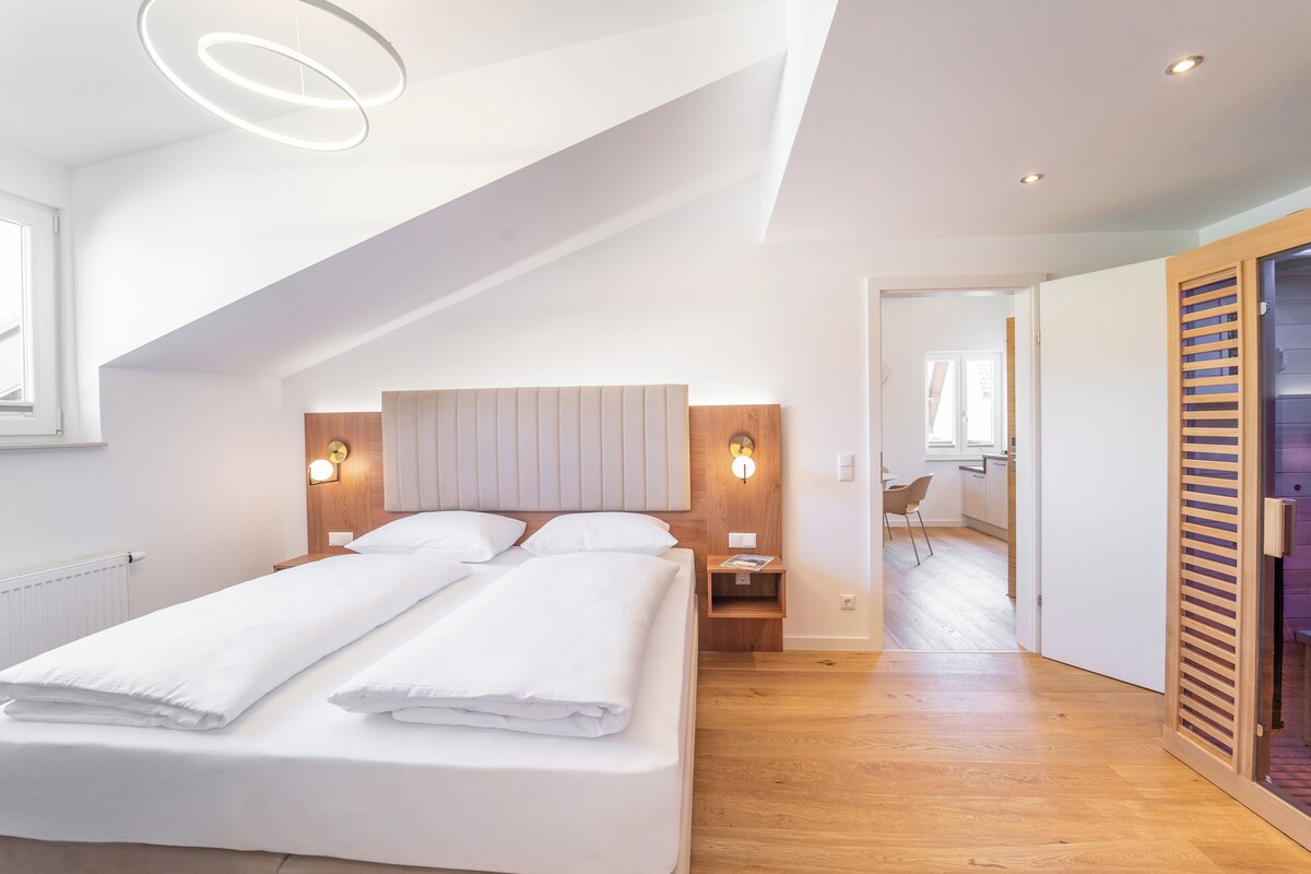 A modern bedroom with a large bed, a wooden headboard, bedside lamps, and a skylight.