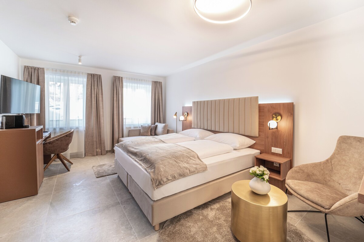 A modern hotel room with a bed, a desk, a chair, and a TV.