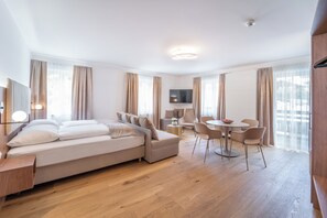 A modern hotel room with a bed, a sofa, a TV, and a dining area with chairs and a table. - das mondsee (Mondsee)