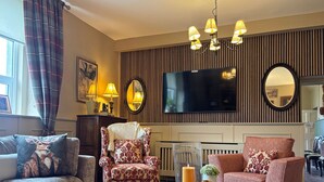 A living room with a sofa, armchair, and ottoman, a flat-screen TV, a fireplace, and a mirror. - Property 472 - Kylemore - sleeps 20 guests  in 11 bedrooms (Kylemore)