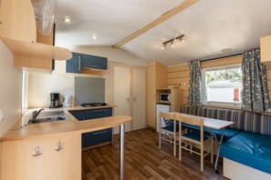 Eine kompakte Küche mit Spüle, Herd und Mikrowelle, ein Essbereich mit Tisch und Stühlen sowie ein Fenster mit Vorhängen.