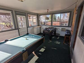 A pool table with a ball, a foosball table, and a window with a view of the outside. - NEW! Spacious Sturgis Rally Rental (Spearfish)