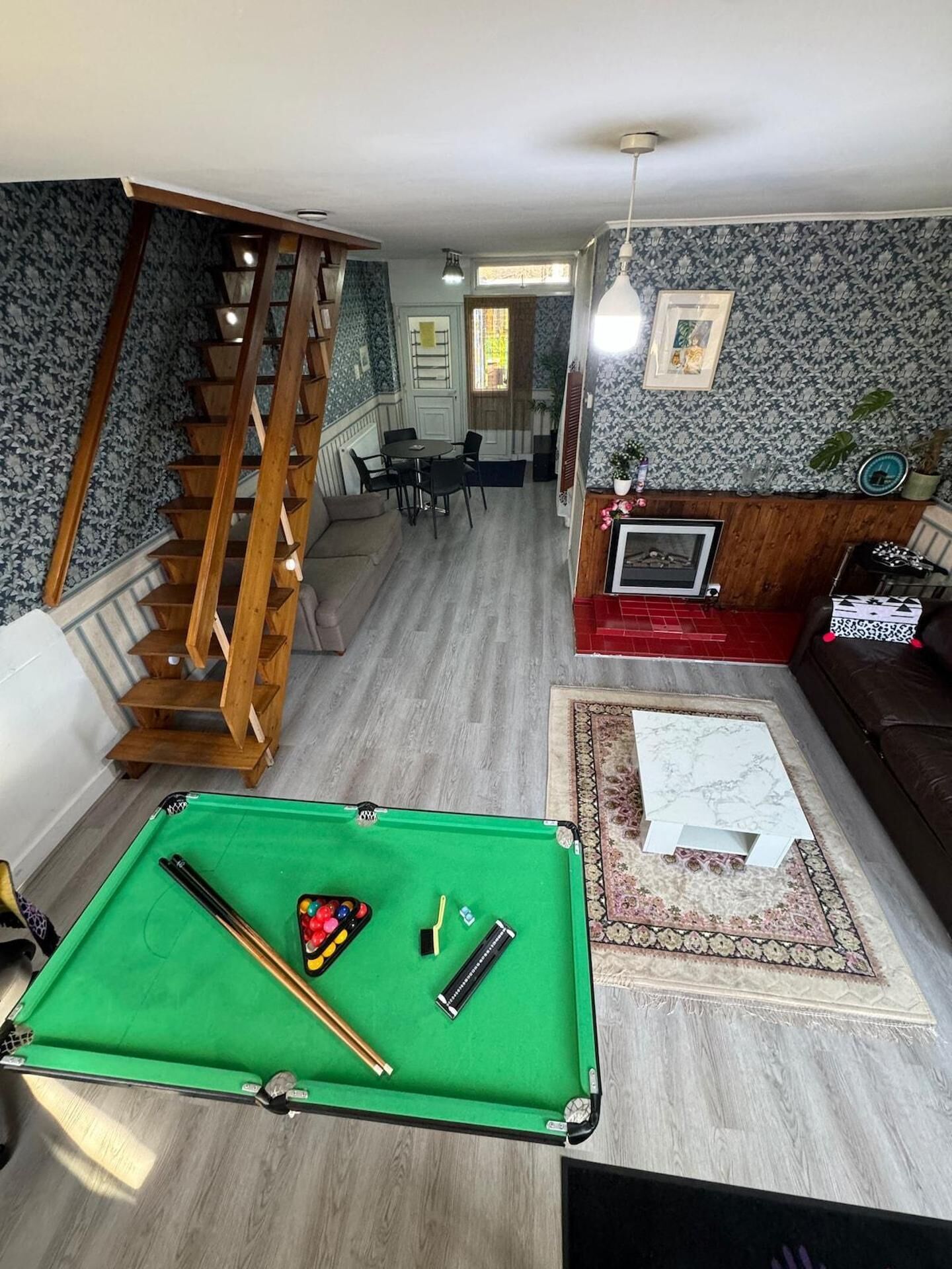 A living room with a pool table, a sofa, a staircase, and a dining area.