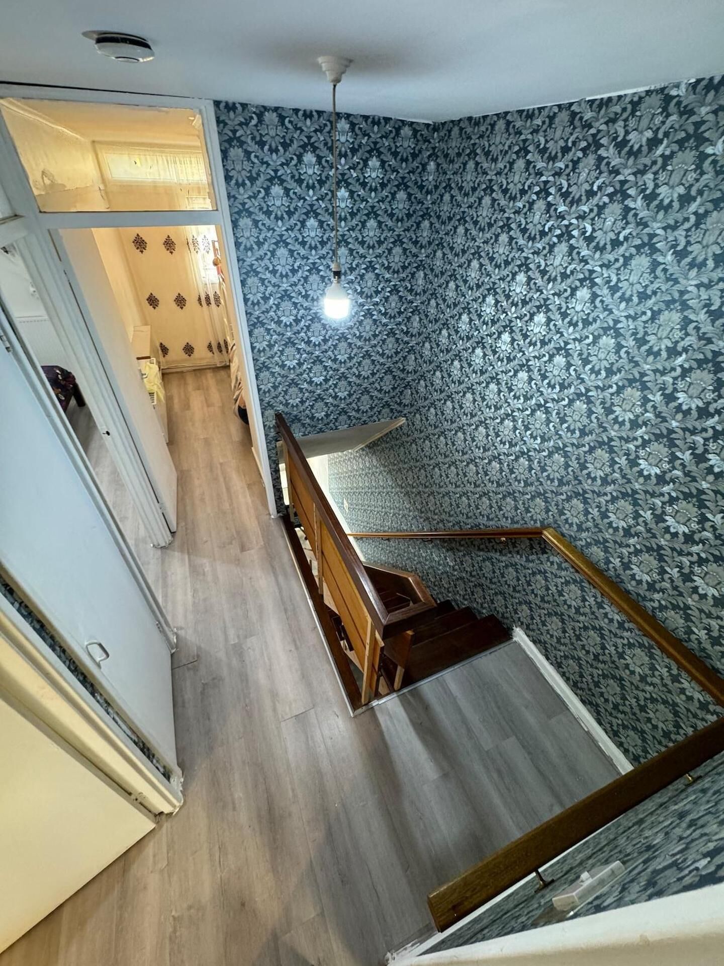 Una escalera con papel tapiz estampado, un banco de madera y una lámpara.