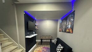 A room with a staircase, a flat-screen TV mounted on a wall, a foosball table, a black sofa with checkered pillows, and a small white table. - 4BR Beautiful Gardner Getaway Game Room Central Location Sleeps 10 (Gardner)