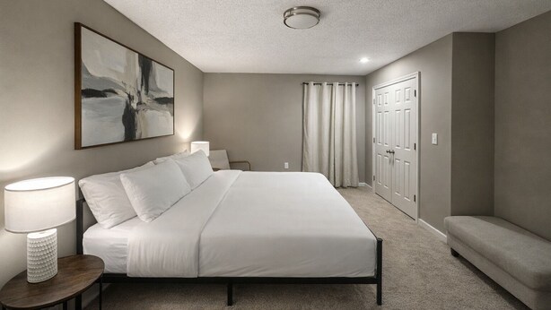 A bedroom with a bed, bedside lamps, a painting, a door, and a bench. - 4BR Beautiful Gardner Getaway Game Room Central Location Sleeps 10 (Gardner)