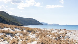 Ein Strand mit Dünen, einem klaren Himmel und fernen Bergen.