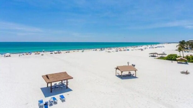 A beach with sun loungers, a covered seating area, and umbrellas. - Coastal Oasis on Siesta Key: 1BR Condo + Boat Dock Access (Sarasota)