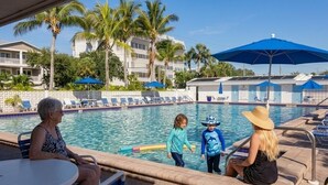 A pool area with lounge chairs, palm trees, and a building in the background. - Coastal Oasis on Siesta Key: 1BR Condo + Boat Dock Access (Sarasota)
