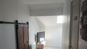 A narrow hallway with a sliding door, a television on a wooden stand, and a small table. - The Gartempe Cottage (Saint-Sornin-la-Marche)