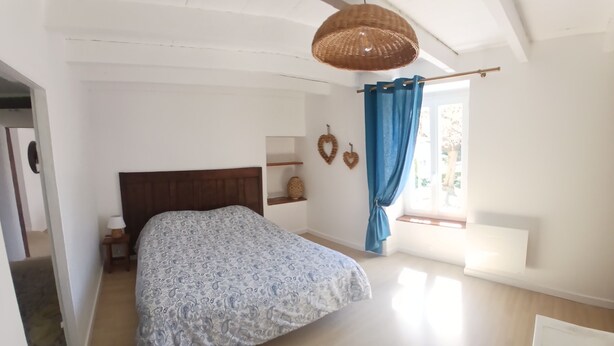 A bedroom with a bed, a nightstand, a wicker ceiling light, a window with blue curtains, and a view of the outdoors. - The Gartempe Cottage (Saint-Sornin-la-Marche)