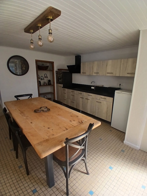 Una cocina con mesa de madera, sillas, un lavamanos y armarios.