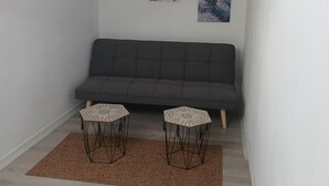 A loft-style room with a grey sofa, two small tables, and two wall-mounted artworks. - The Gartempe Cottage (Saint-Sornin-la-Marche)