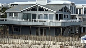 Een huis aan de kust met een balkon, grote ramen en een overdekt terras.
