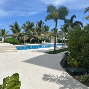 Área de piscina com palmeiras, cadeiras de descanso e céu limpo.