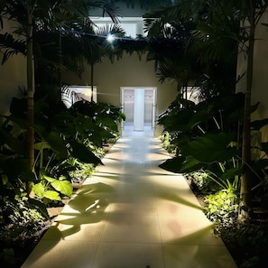 A corridor with tiled flooring, surrounded by lush greenery and palm trees, leading to a door with a glass panel. - Bright and Breezy Punta Cana Escape - Modern (Punta Cana)