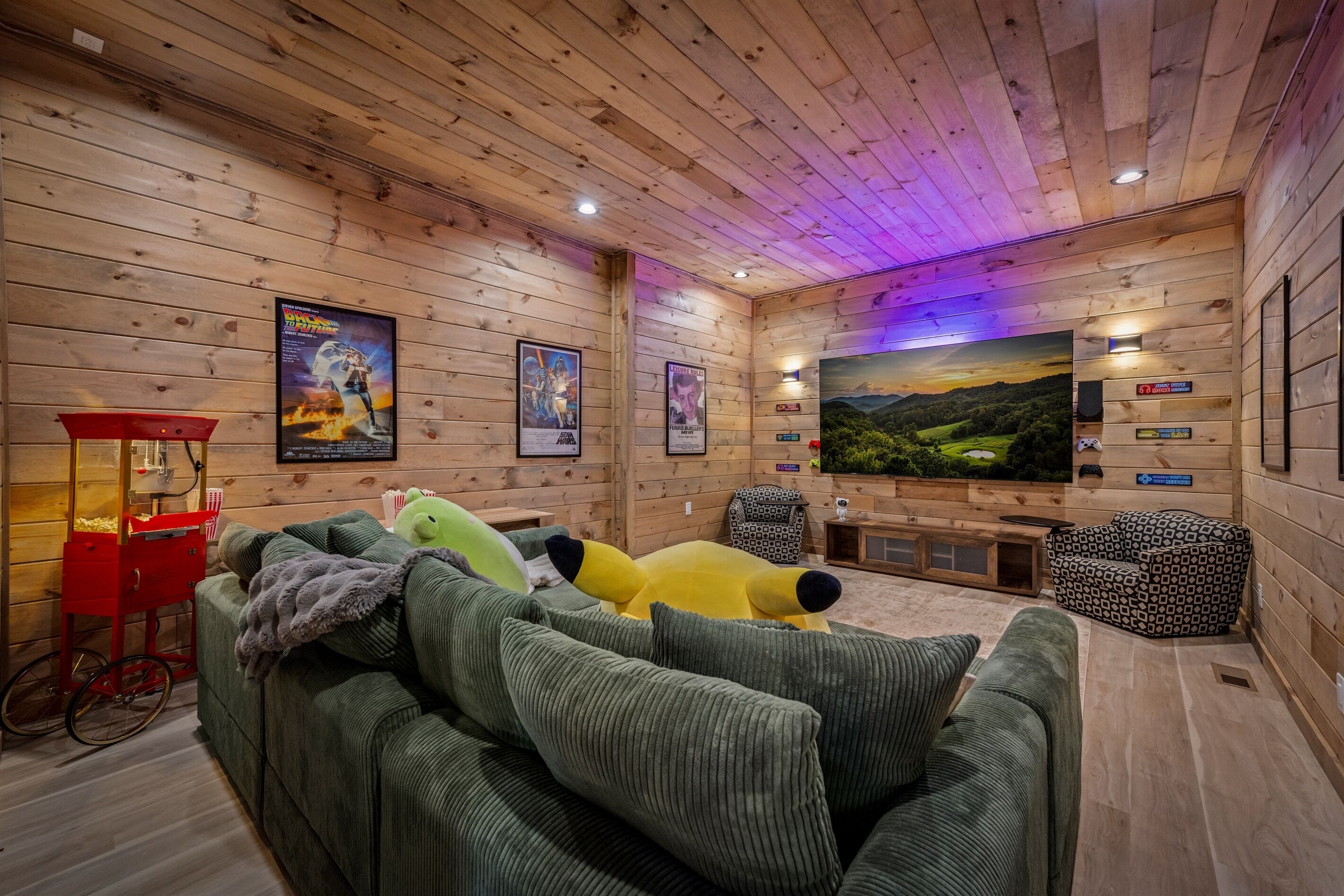 A cozy room with wooden walls, a green sofa, a red popcorn machine, and a large poster of a movie.