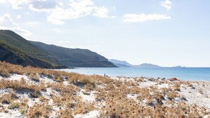 Une plage avec des dunes de sable, un ciel dégagé et des montagnes à l’horizon.