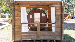 A wooden cabin with a door, a small porch, and a slide in the background. - Mobile Home 'Village Camping De L'ostriconi 20': Sea View, Shared Pool & Wi-Fi (Palasca)