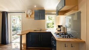 A modern kitchen with a central island, built-in cabinets, a stove, and a fan. - Mobile Home 'Village Camping De L'ostriconi 20': Sea View, Shared Pool & Wi-Fi (Palasca)