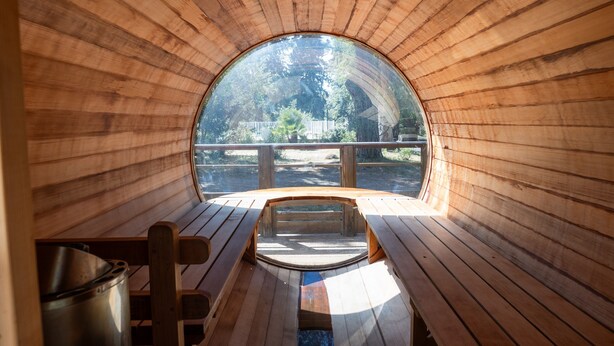A wooden interior with a circular window, wooden benches, and a metal pot. - Mobile Home 'Village Camping De L'ostriconi 20': Sea View, Shared Pool & Wi-Fi (Palasca)