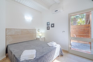 A bedroom with a bed, bedside table, lamp, wall art, and a sliding glass door to an outdoor area.